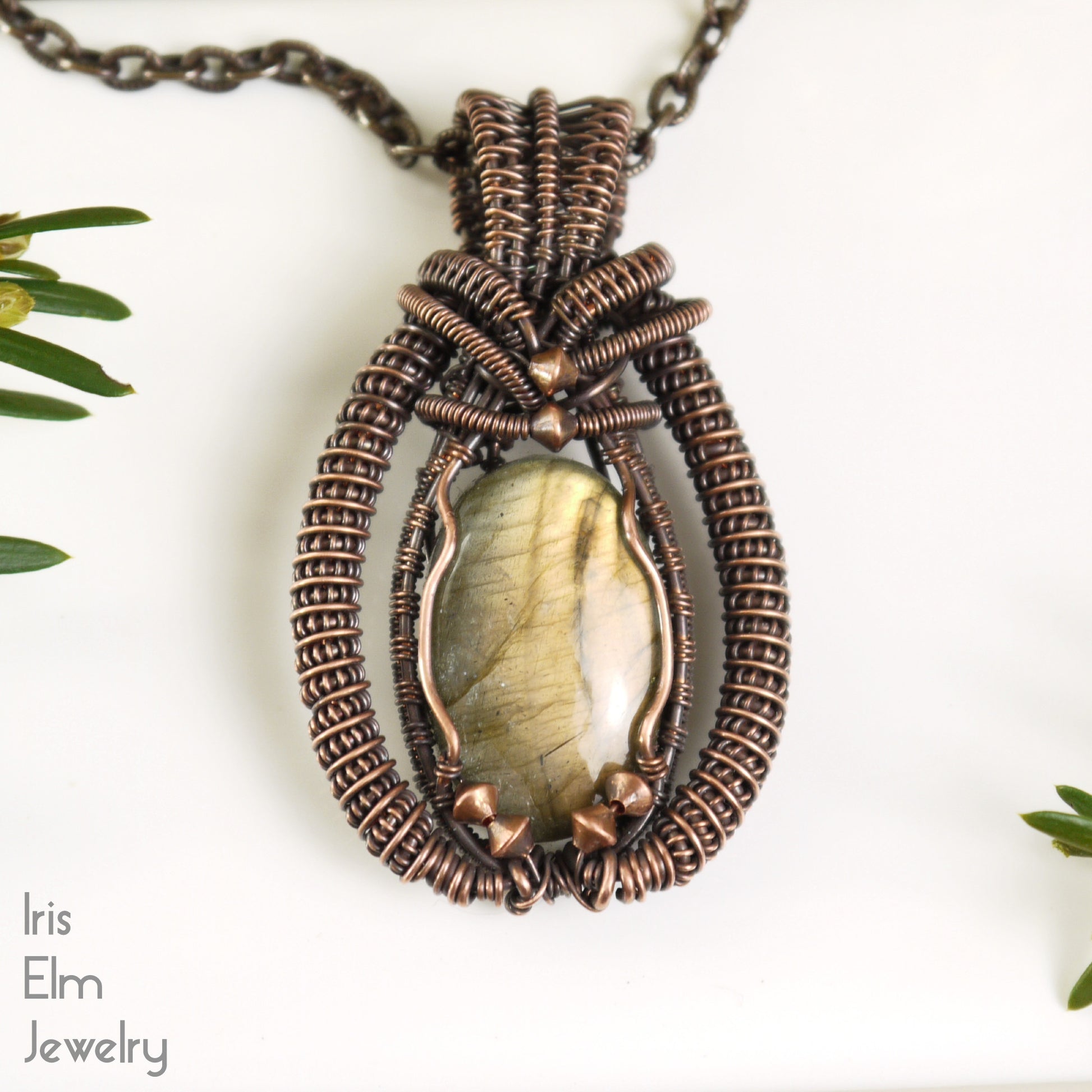 Jewelry pendant with an iridescent labradorite green stone and copper wire wrapping on a white background
