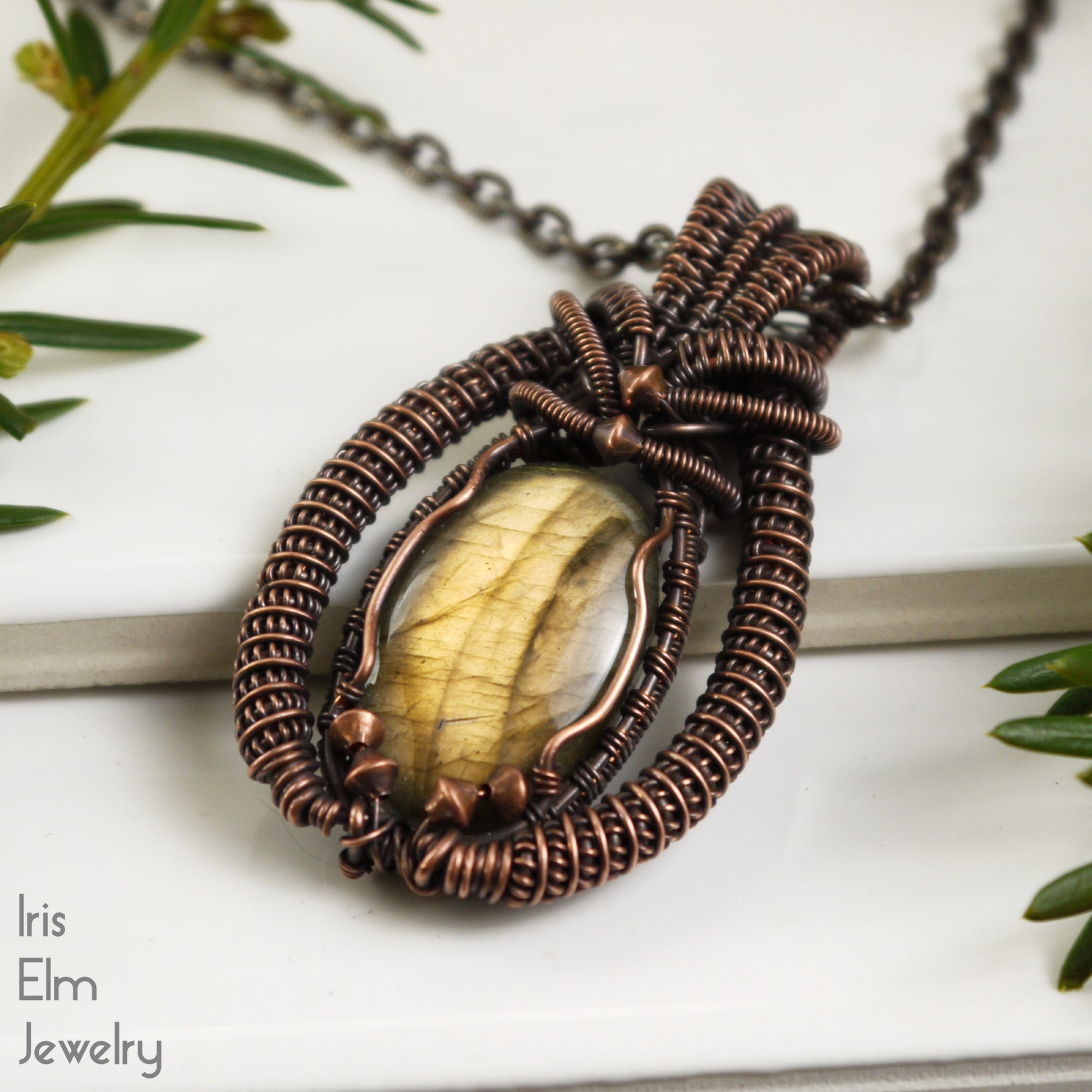 Copper-wrapped handcrafted pendant with a central labradorite stone on a white background with greenery