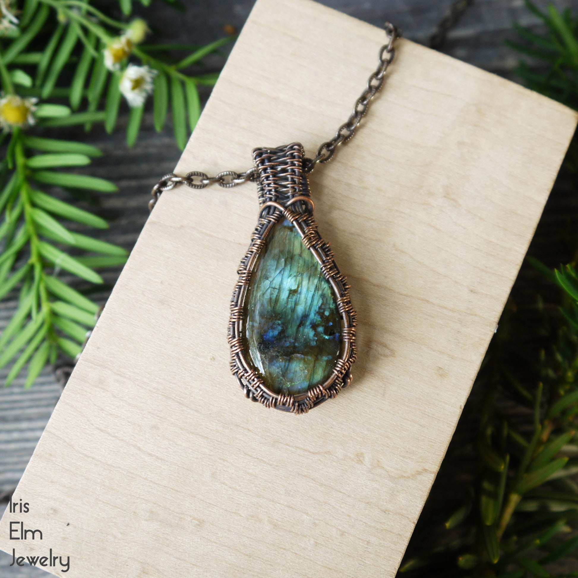 Labradorite teardrop copper wire woven pendant necklace on a wooden surface with greenery in the background