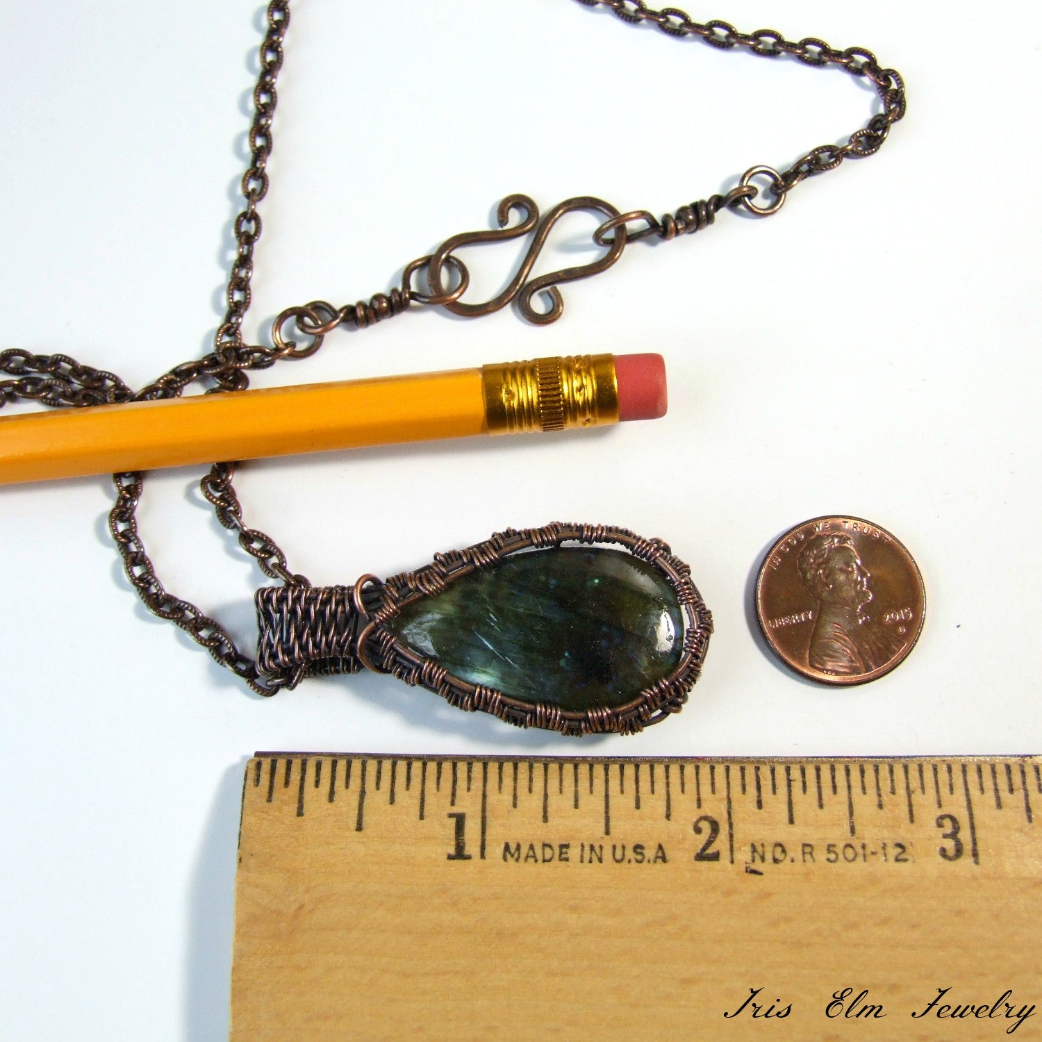 Necklace with a green stone pendant next to a pencil and penny for scale on a white background
