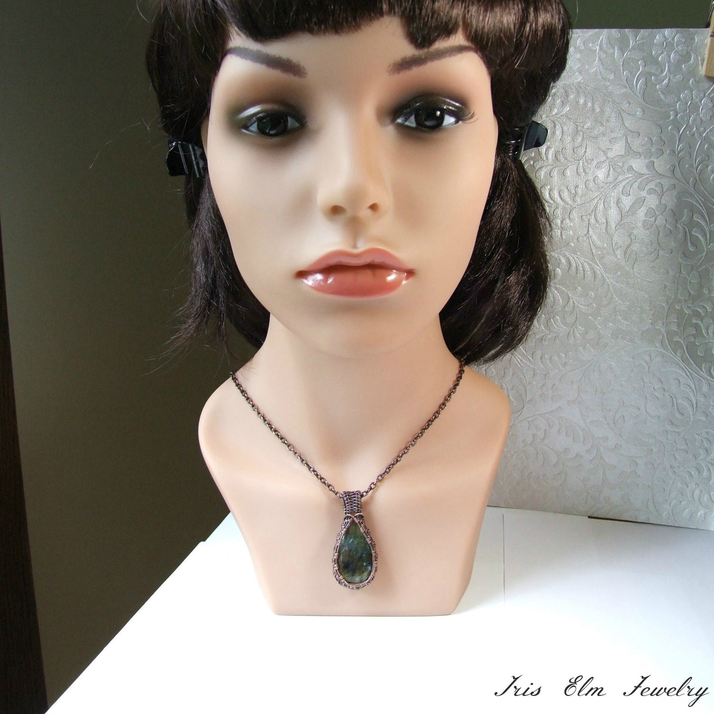 Mannequin head with a labradorite copper wire wrapped pendant necklace on a white surface