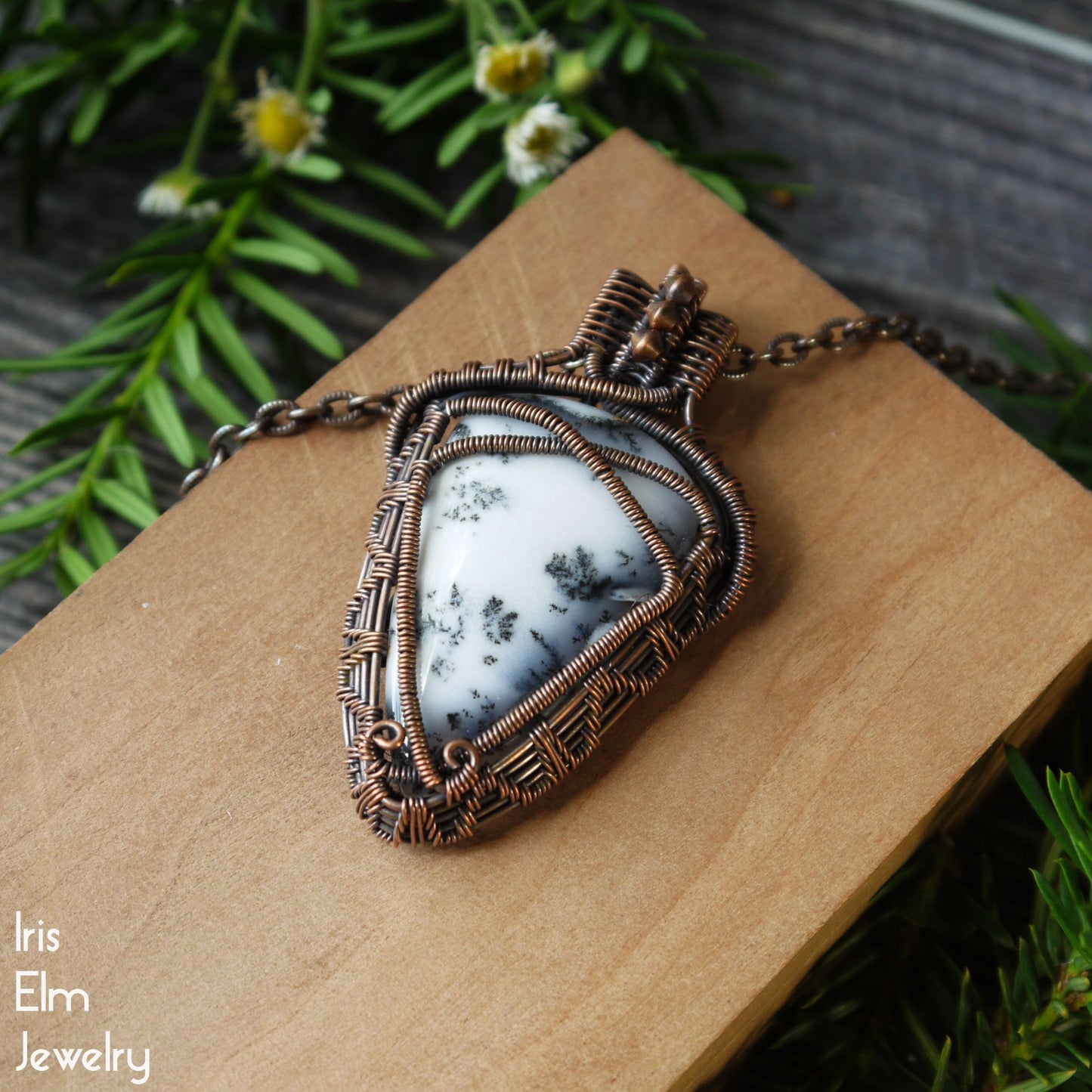 handmade Jewelry pendant with a natural dendritic agate stone on a wooden surface with greenery in the background
