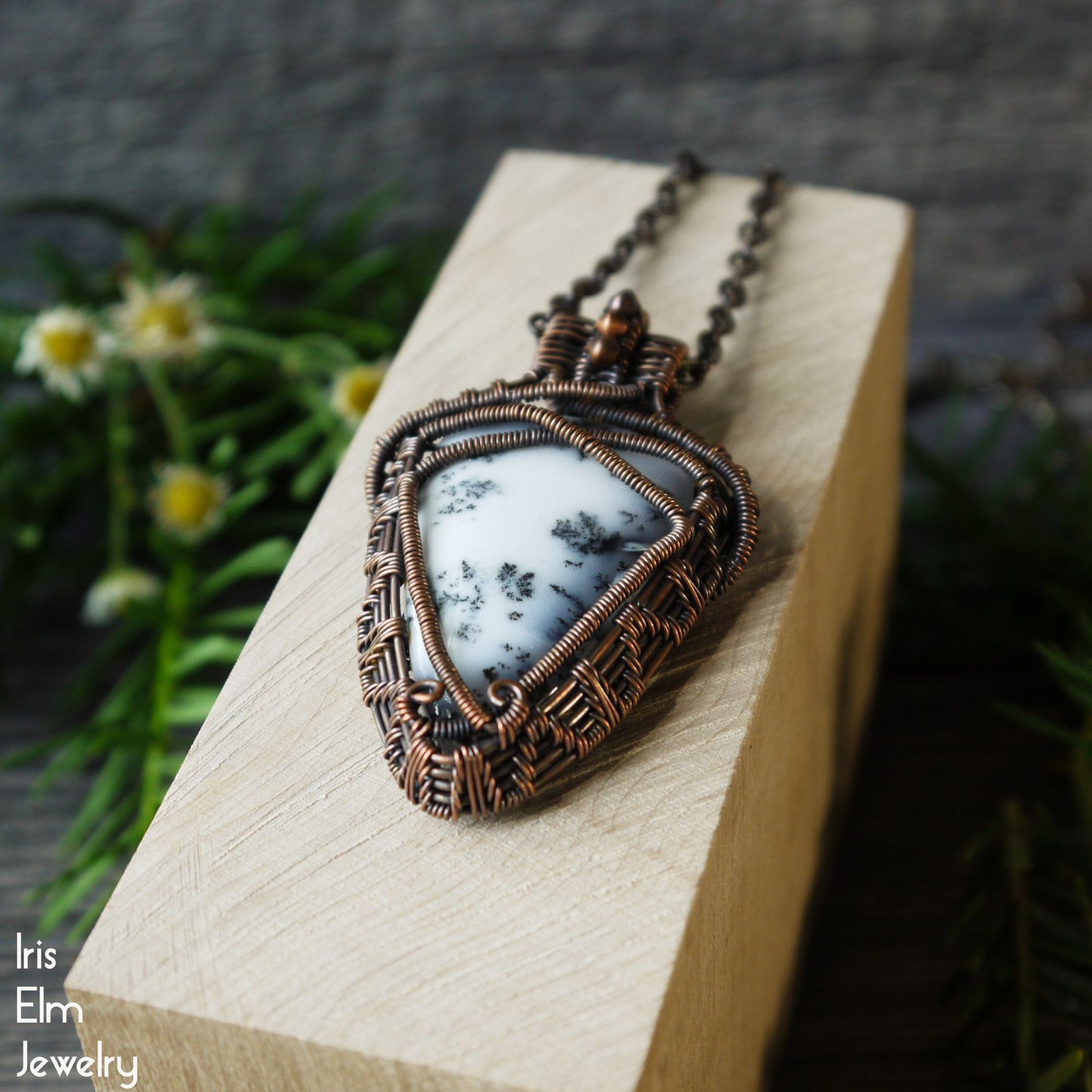 copper wire wrapped Jewelry pendant with natural white agate stone on a wooden block with blurred greenery in the background