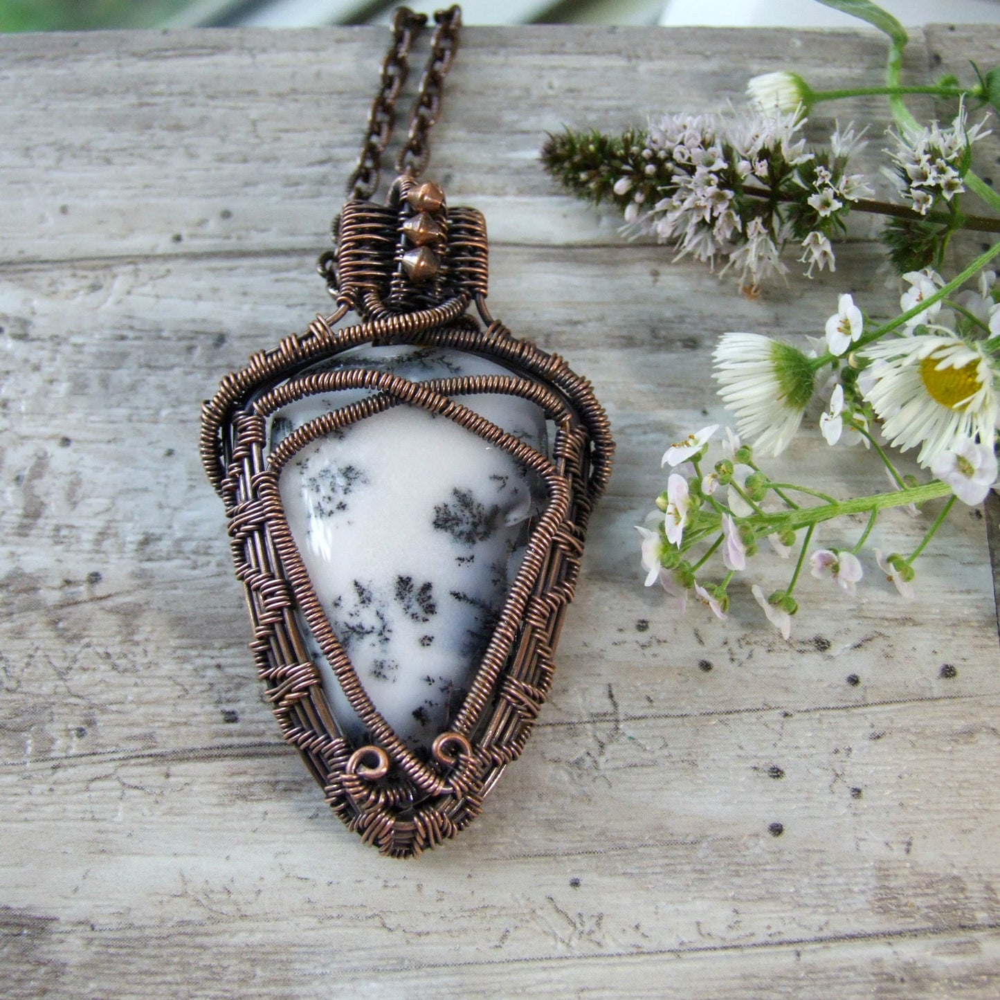 handcrafted Copper-wrapped pendant with a white stone on a wooden surface with flowers