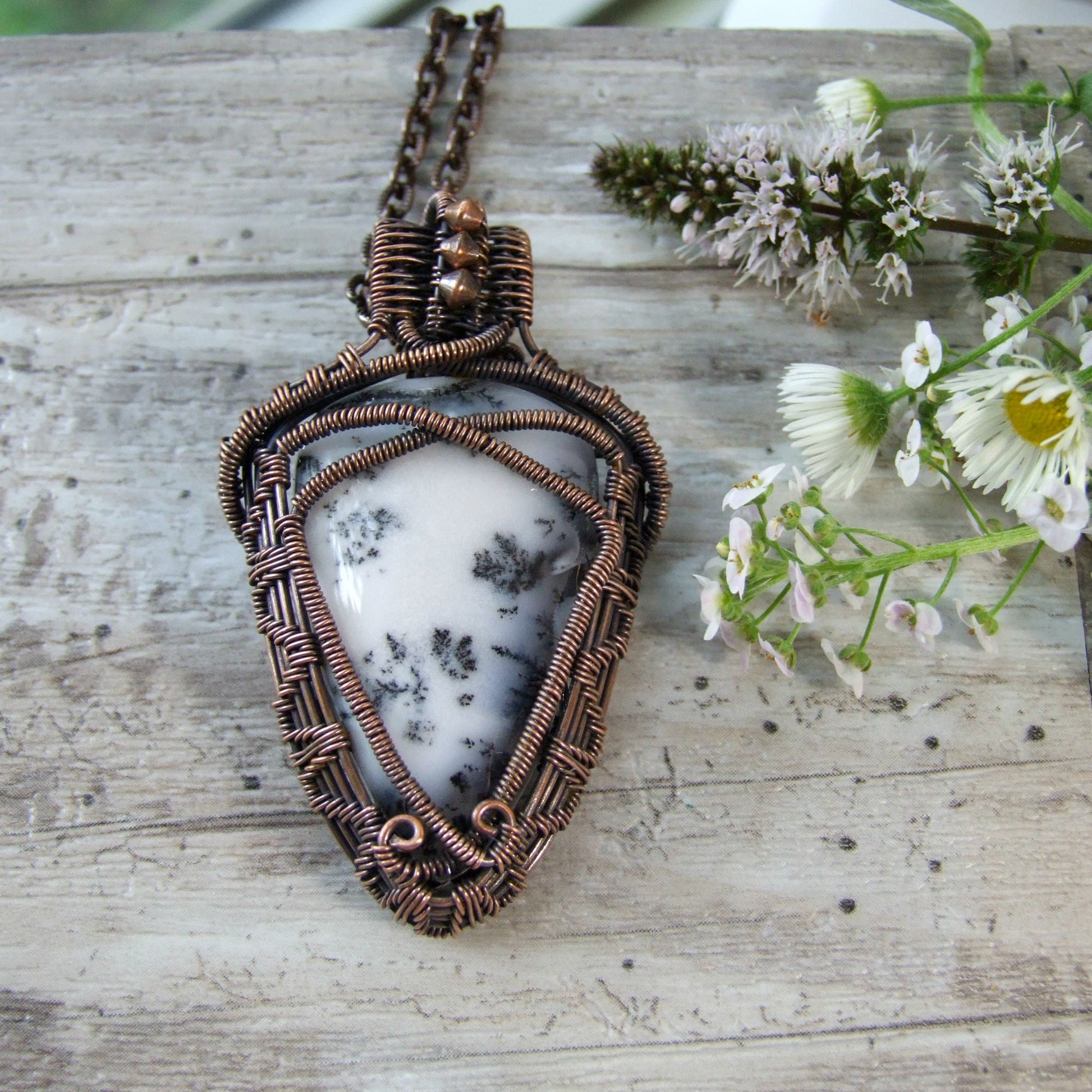 handcrafted Copper-wrapped pendant with a white stone on a wooden surface with flowers