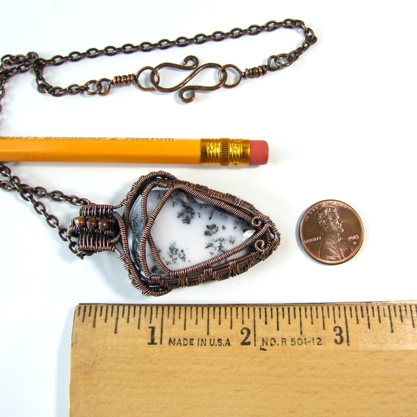 Necklace with a triangular agate pendant next to a pencil and penny on a white background