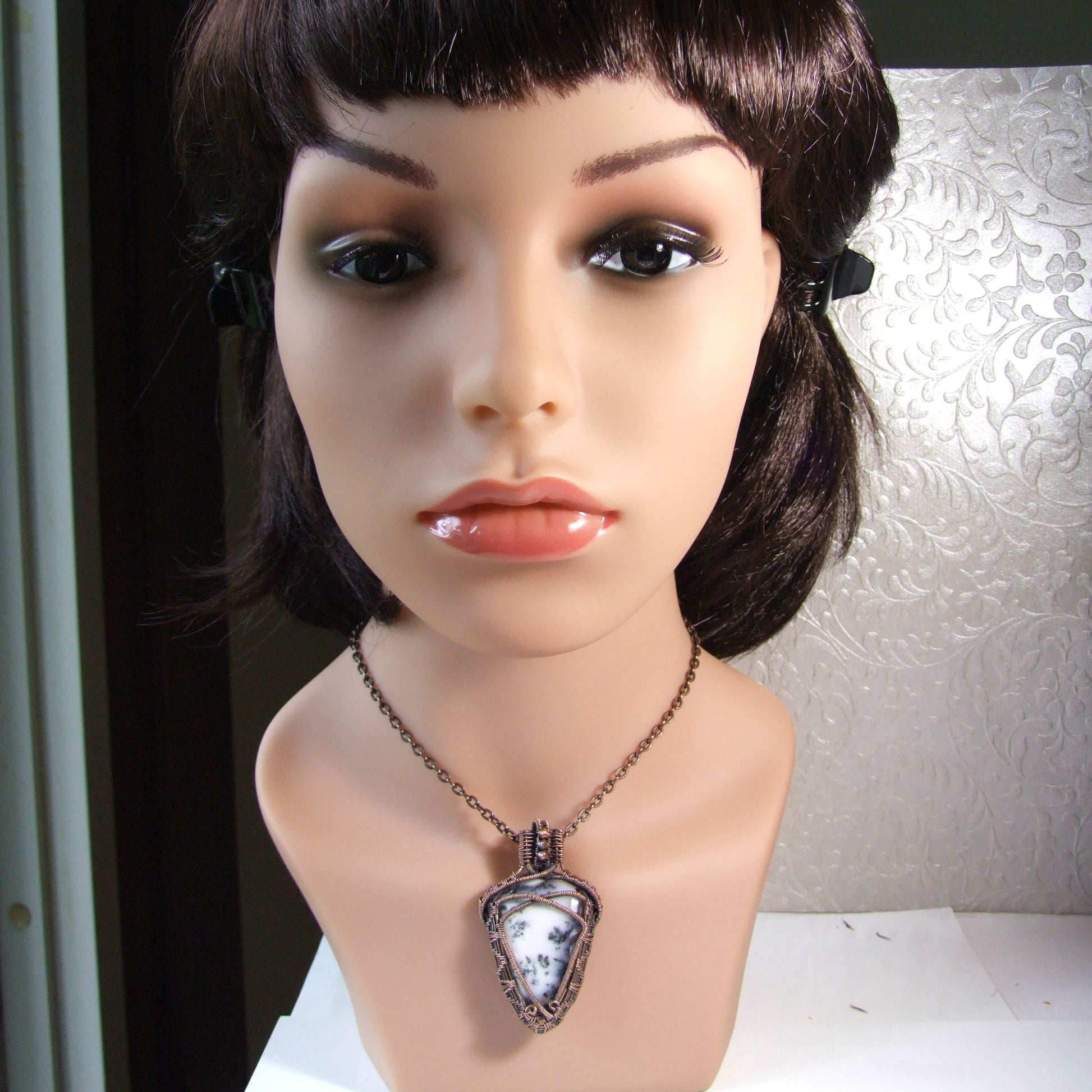 Mannequin head with a white agate copper wire wrapped pendant necklace on a textured wall background