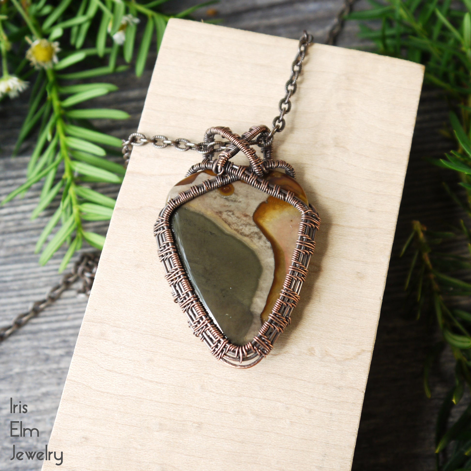 copper wire wrapped Necklace with a artisan handcrafted earth tone jasper pendant on a wooden surface, surrounded by greenery