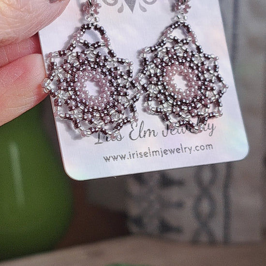 a pair of lilac purple seed bead mandala earrings on a Iris Elm Jewelry branded card held by hand