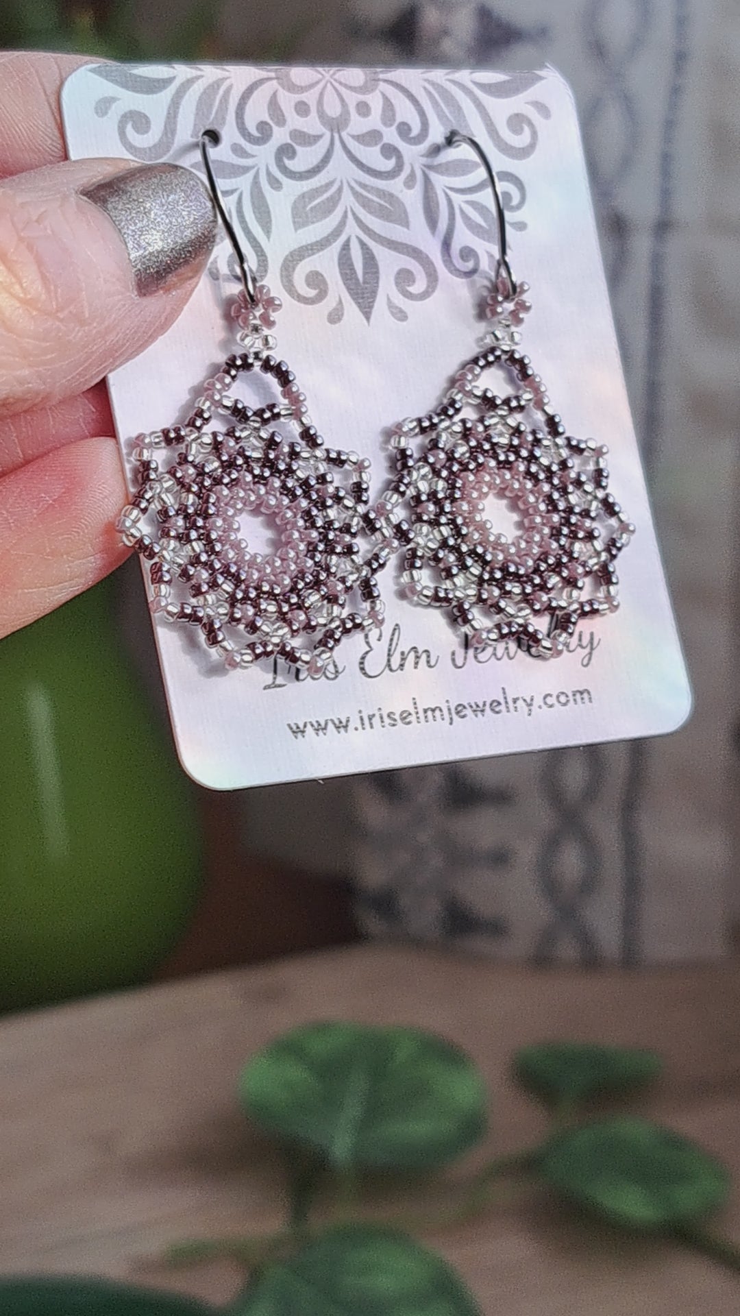 a pair of lilac purple seed bead mandala earrings on a Iris Elm Jewelry branded card held by hand