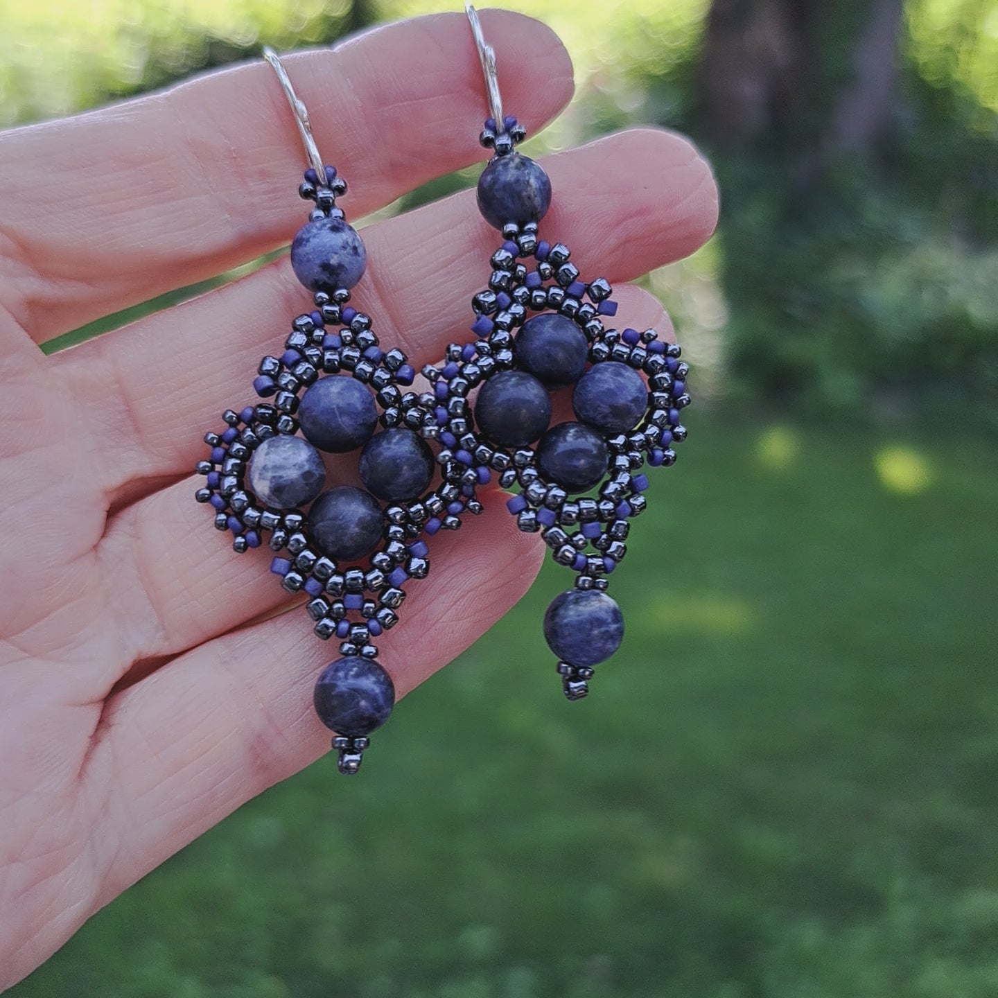 a pair of beadwoven sodalite earrings held in hand in outdoor setting