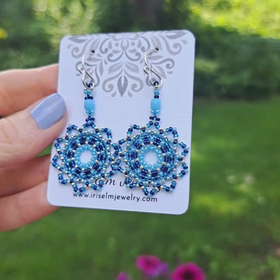 a pair of blue seed bead mandala earrings on a Iris Elm Jewelry branded card held by hand
