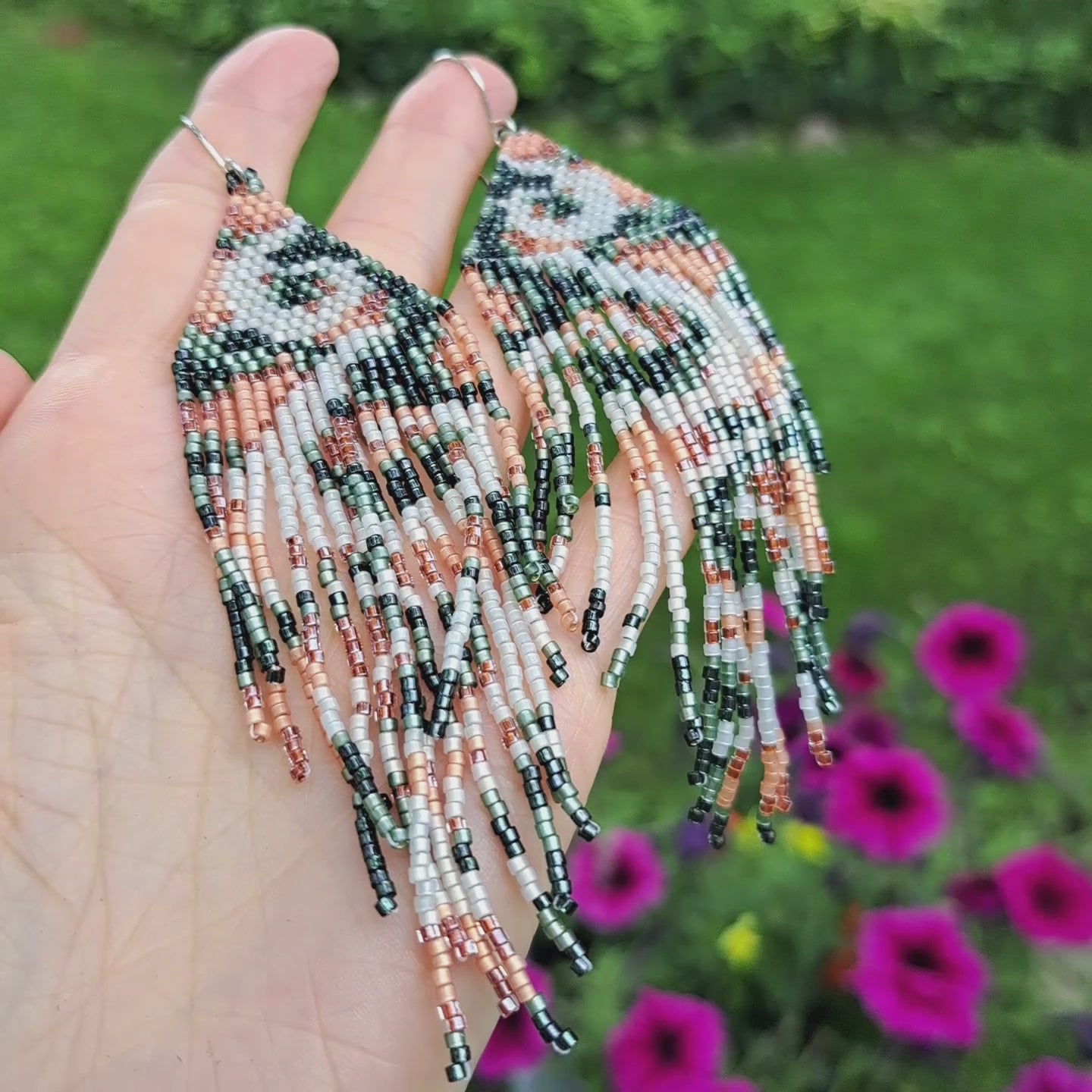 a pair of long fringe seed bead earrings held in hand in outdoor setting