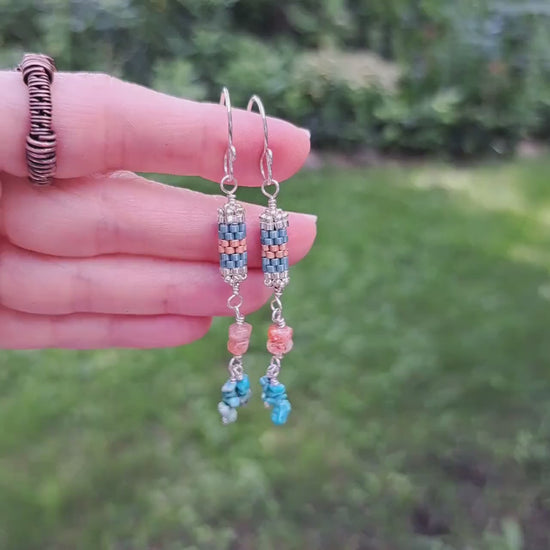 a pair of seed bead beadwork earrings with sunstone and turquoise chip gemstones beaded on sterling silver wire dangling beneath. Earrings are held in hand in outdoor setting
