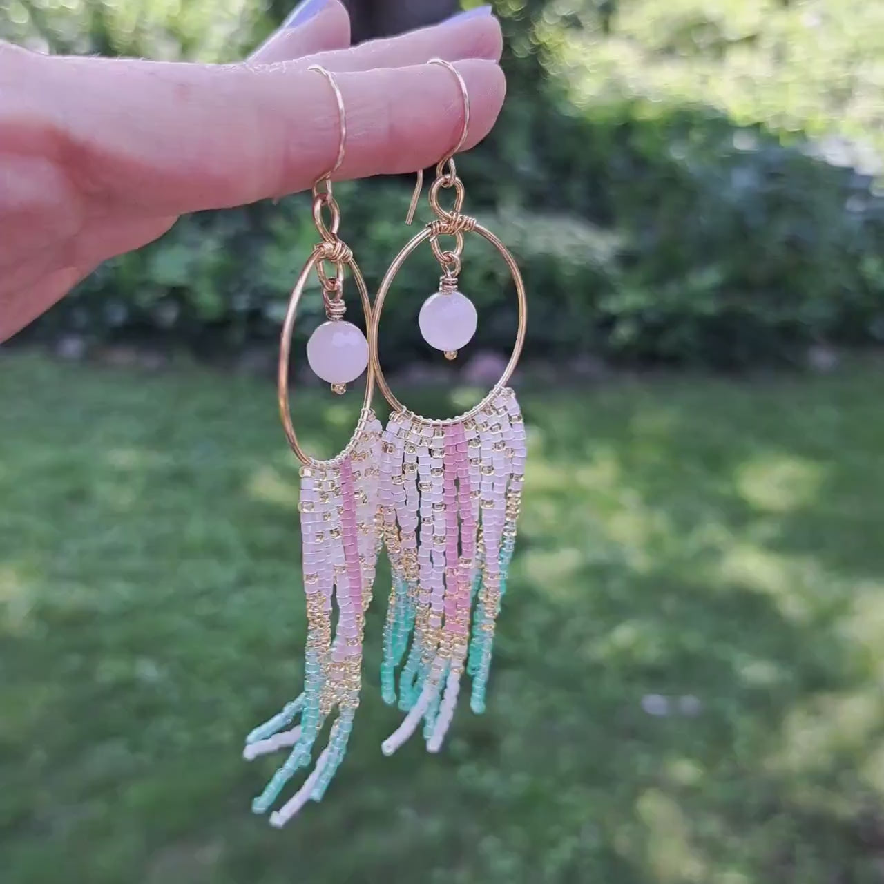 a pair of rose quarts hoop fringe earrings held in hand in outdoor setting