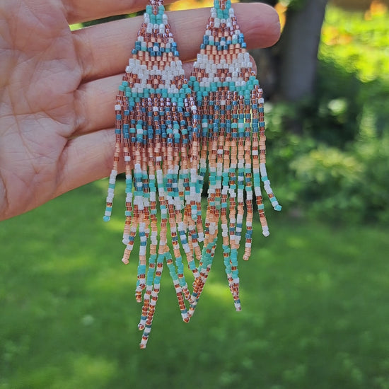 hand holding pair of long bohemian seed bead fringe earrings in outdoor setting