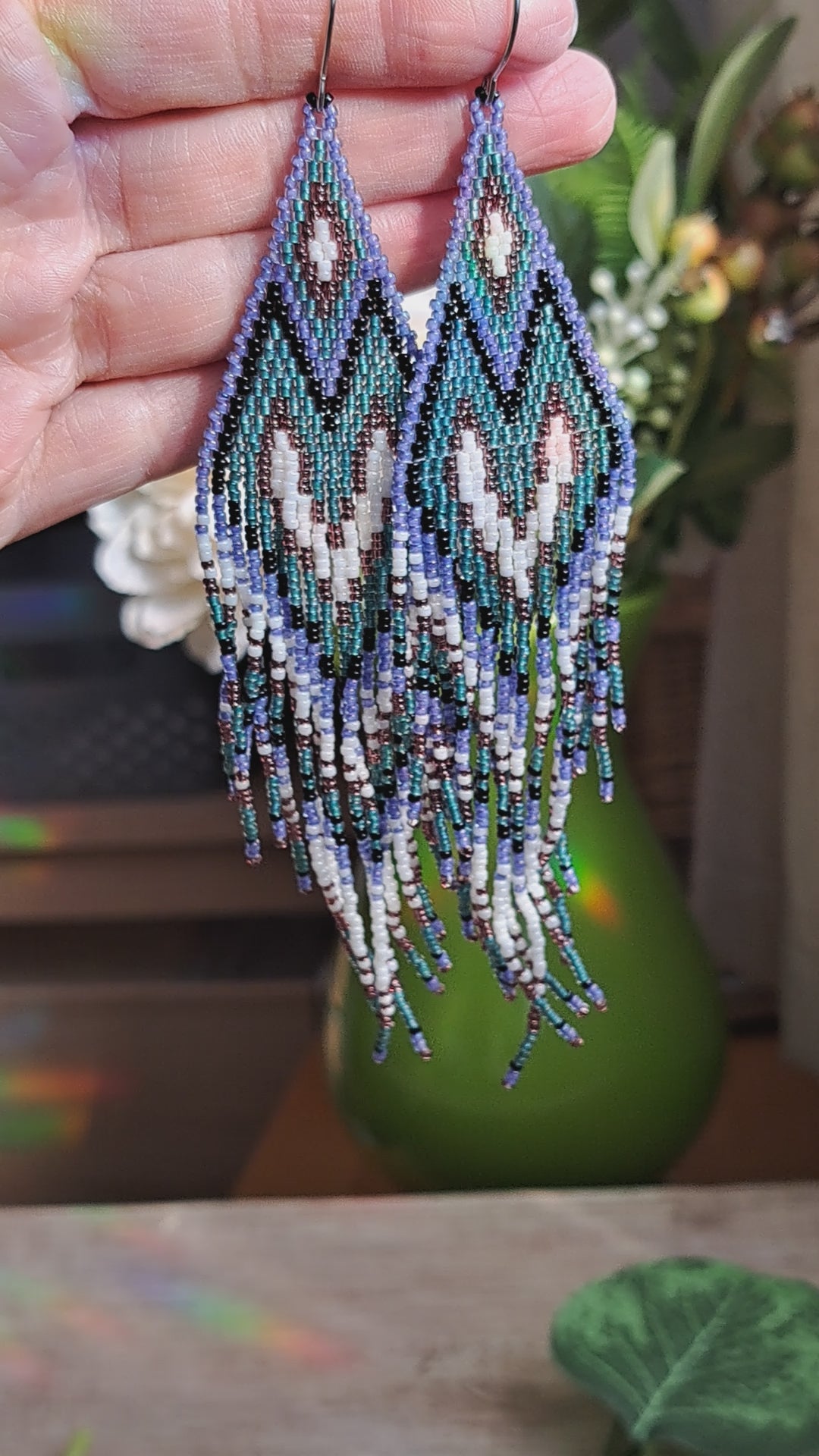 hand holding long purple, teal, black, and white seed bead heart fringe earrings