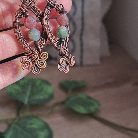 hand holding a pair of copper wire wrapped green and mauve jasper stone dangle earrings