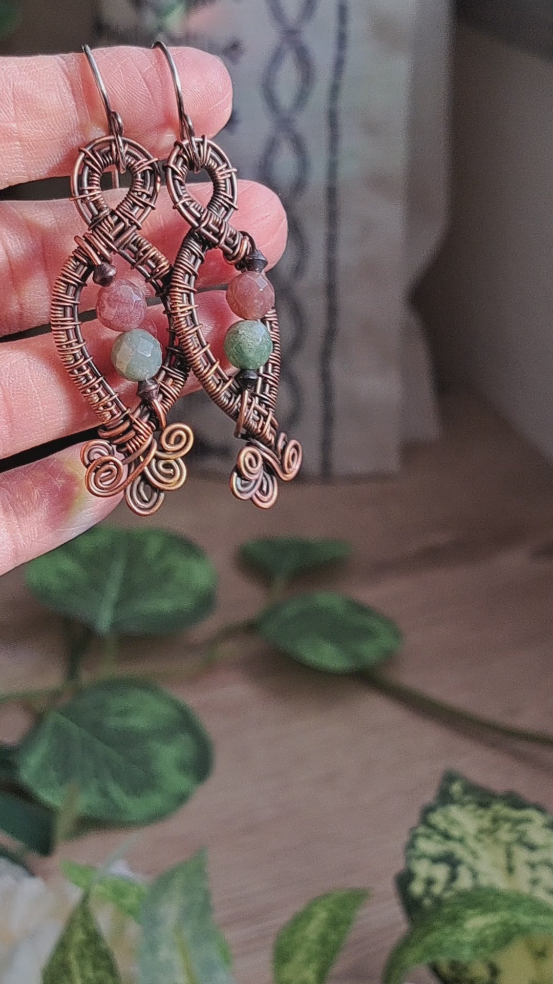 hand holding a pair of copper wire wrapped green and mauve jasper stone dangle earrings