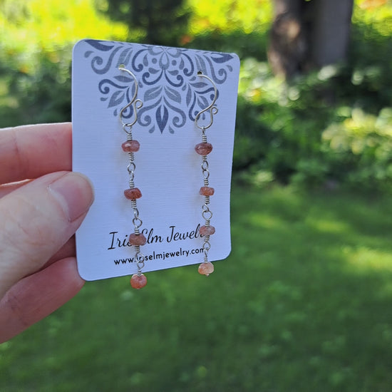 a pair of sterling silver dangle sunstone earrings on Iris Elm Jewelry branded card held by hand
