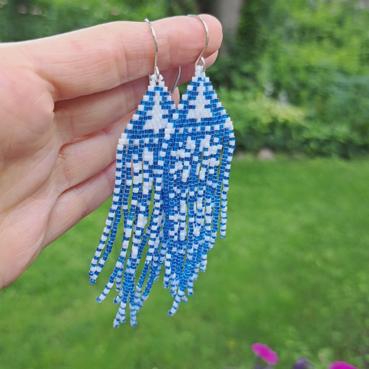 hand holding blue and white snowflake seed bead fringe earrings in outdoor setting