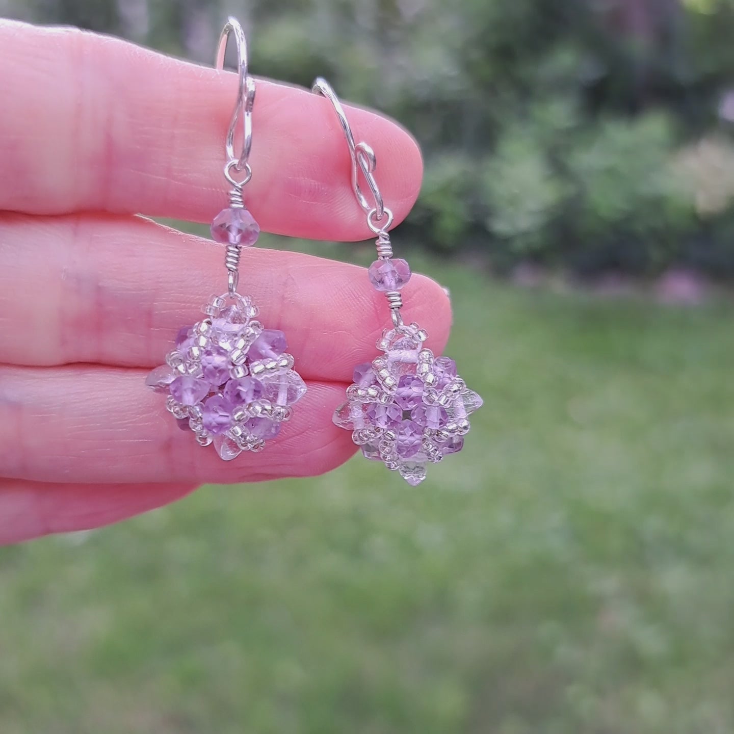 a pair of sterling silver beadwork gemstone purple amethyst and clear quartz crystal earrings held by hand
