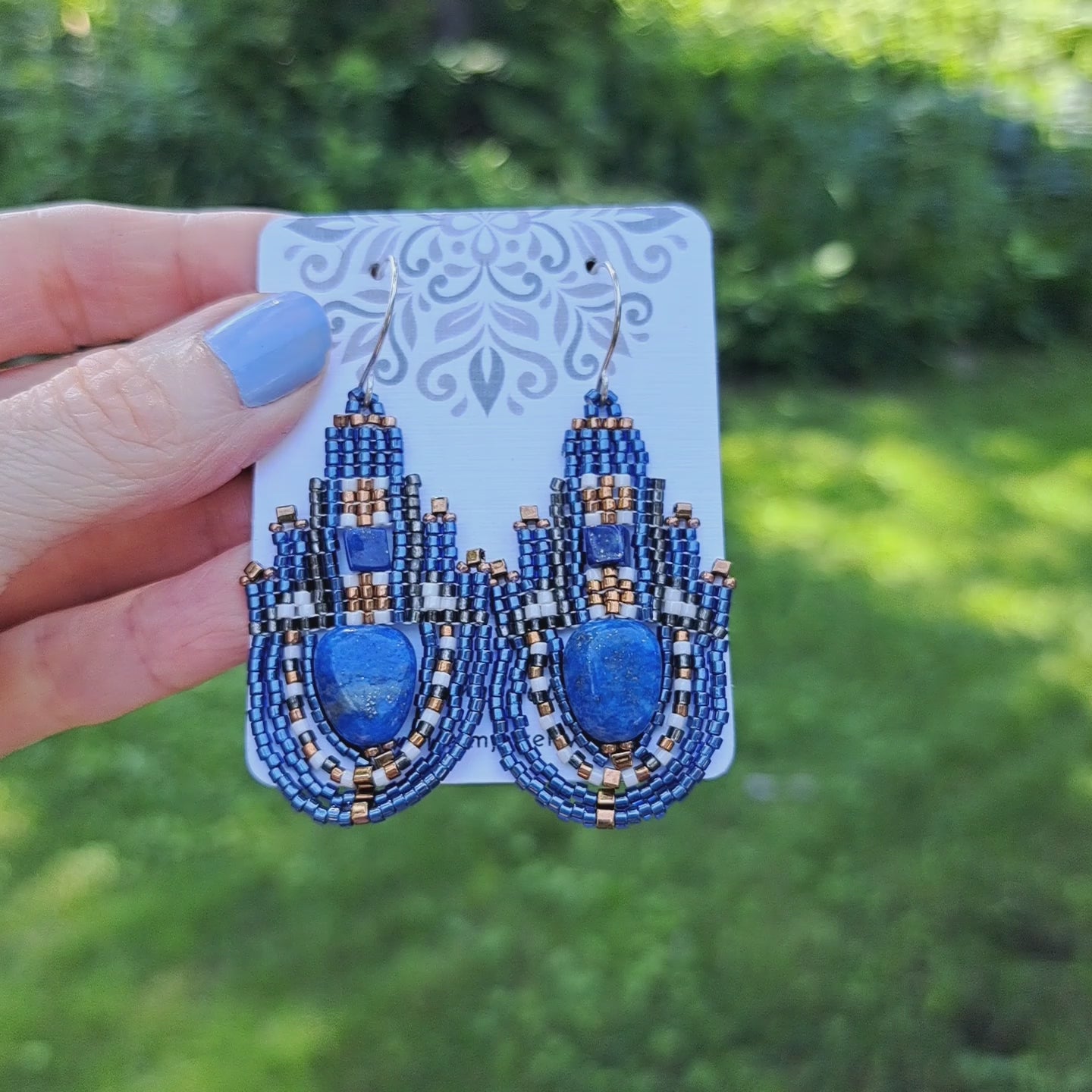 a pair of blue lapis stone and seed bead earrings on branded Iris Elm Jewelry card held by hand