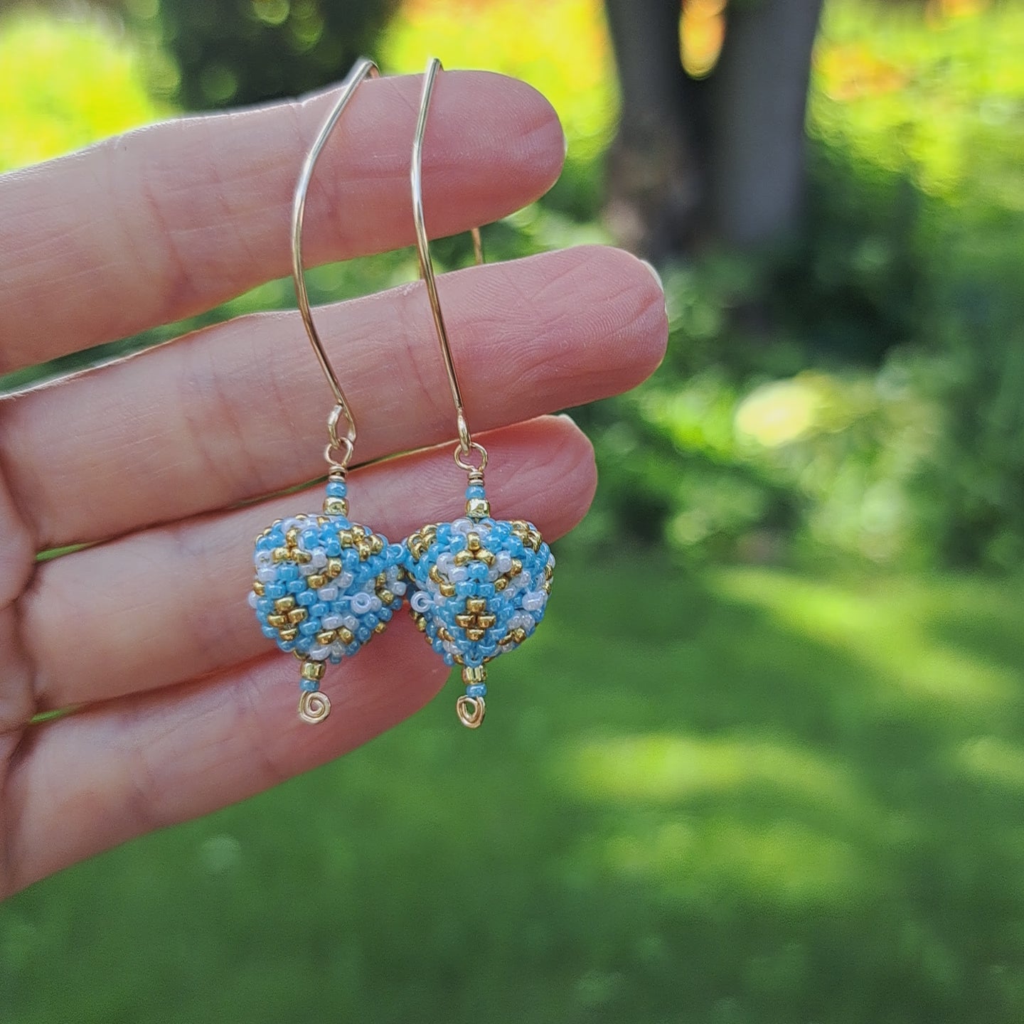 hand holding pair of seed bead triangle earrings with light blue, white, and gold beads dangling from marquise ear wires