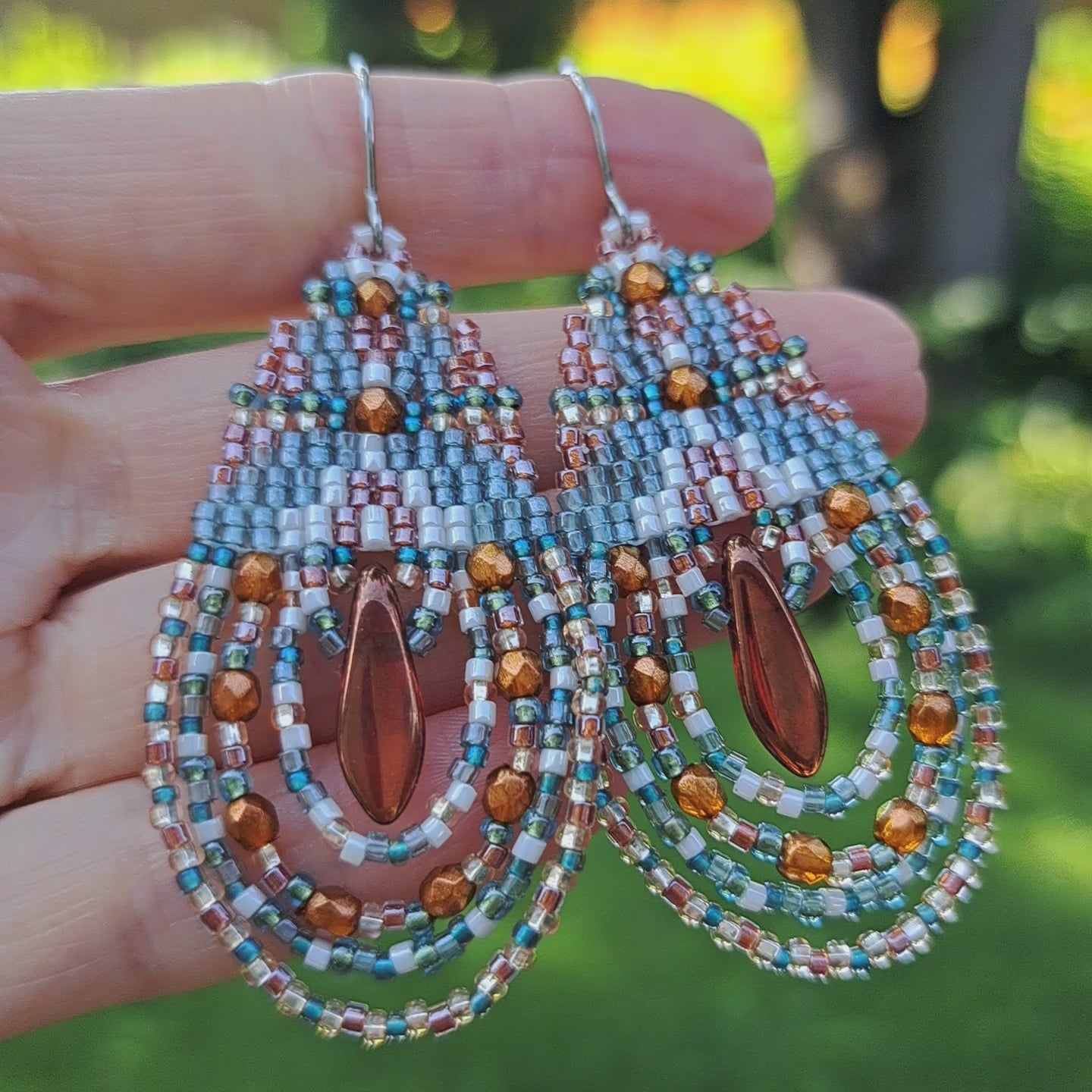 hand holding pair of bohemian glass teardrop earrings in outdoor setting