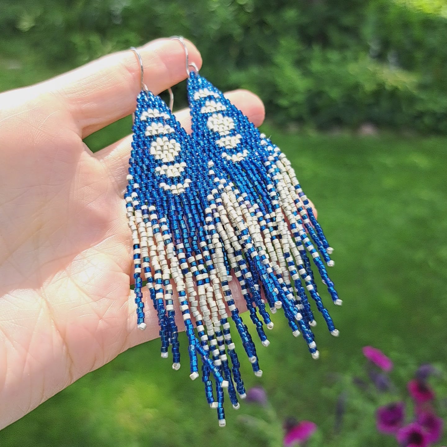 hand holding blue long seed bead moon phase fringe earrings in outdoor setting
