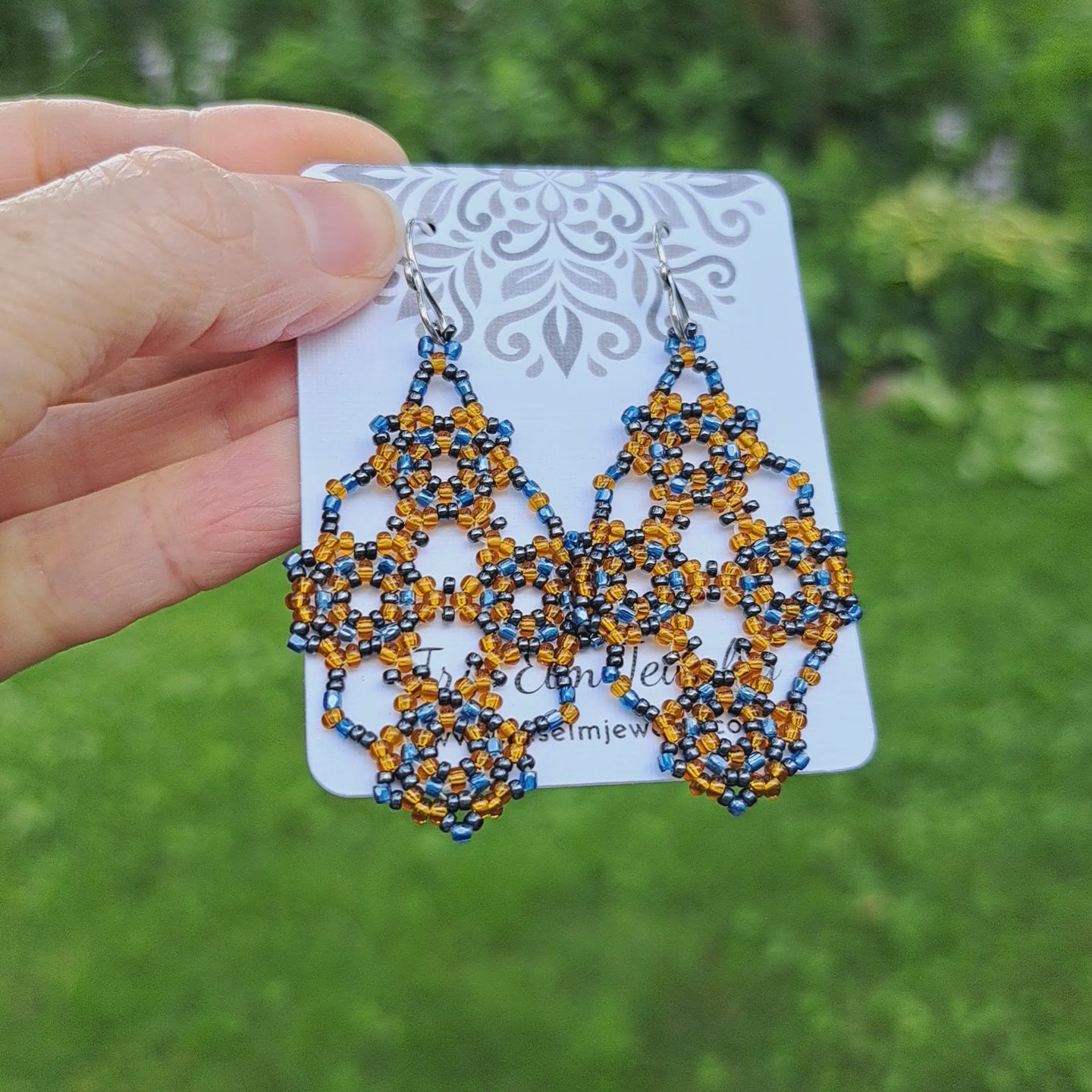 amber orange and blue seed bead lattice earrings on Iris Elm Jewelry card held by hand