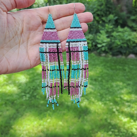 a pair of long seed bead fringe earrings with a pink and mint green plaid pattern held in hand in outdoor setting