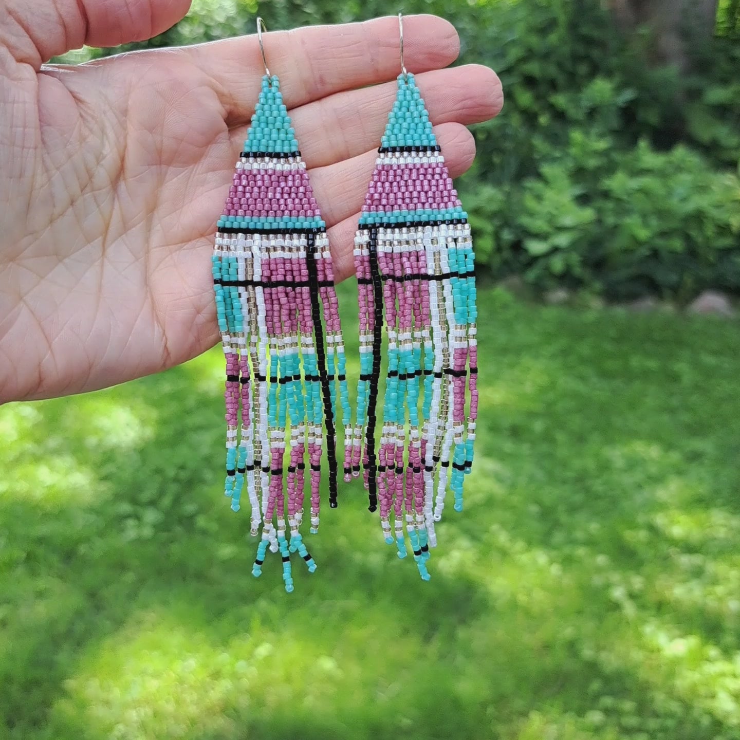 a pair of long seed bead fringe earrings with a pink and mint green plaid pattern held in hand in outdoor setting
