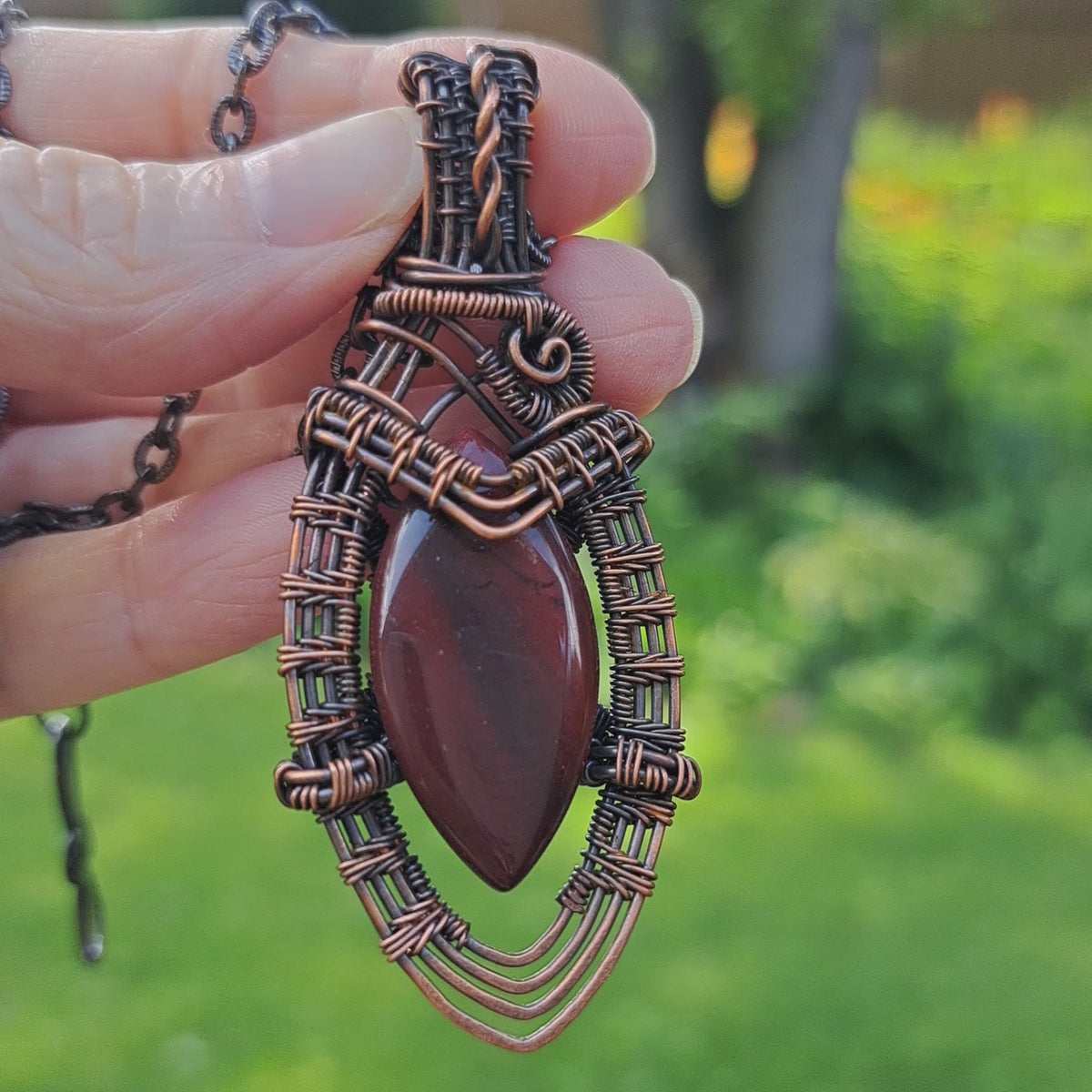 hand holding and intricately copper wire wrapped red jasper marquise shaped pendant necklace