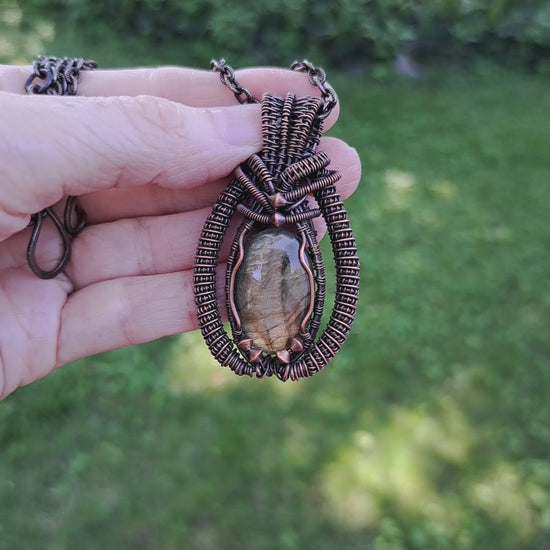 hand holding an intricately wire wrapped coiled labradorite pendant necklace