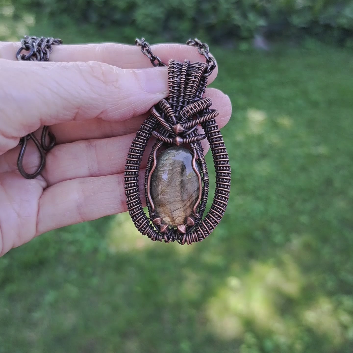 hand holding an intricately wire wrapped coiled labradorite pendant necklace