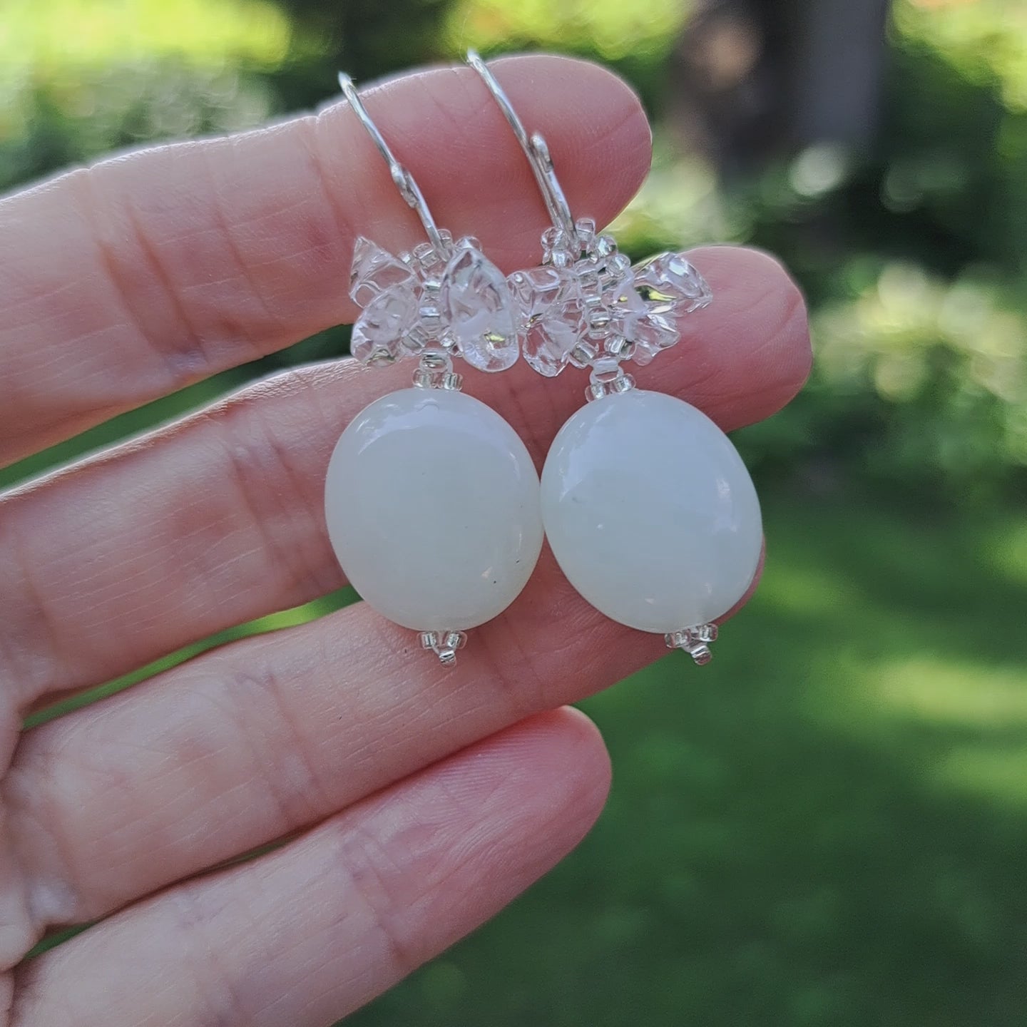 hand holding pair of beaded earrings with pale seafoam green oval shaped serpentine jade stones with clear quartz crystal stones beaded above