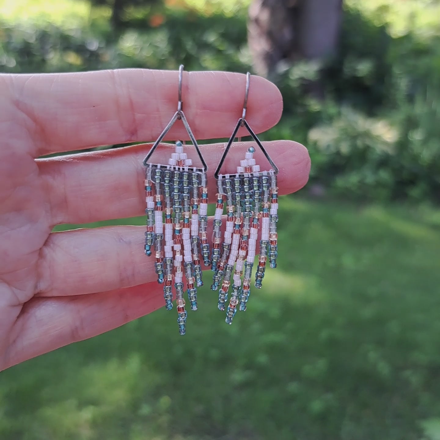 hand holding pair of small fringe earrings with triangle tops and turquoise, white, and copper seed beads