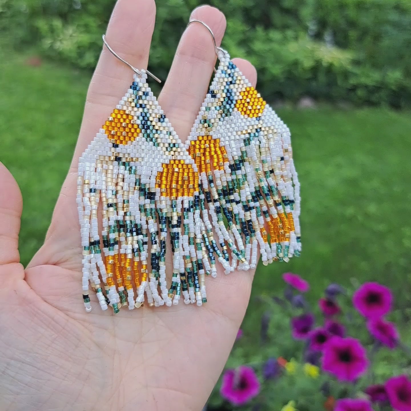 hand holding pair of seed bead orange floral patterned fringe earrings in outdoor setting