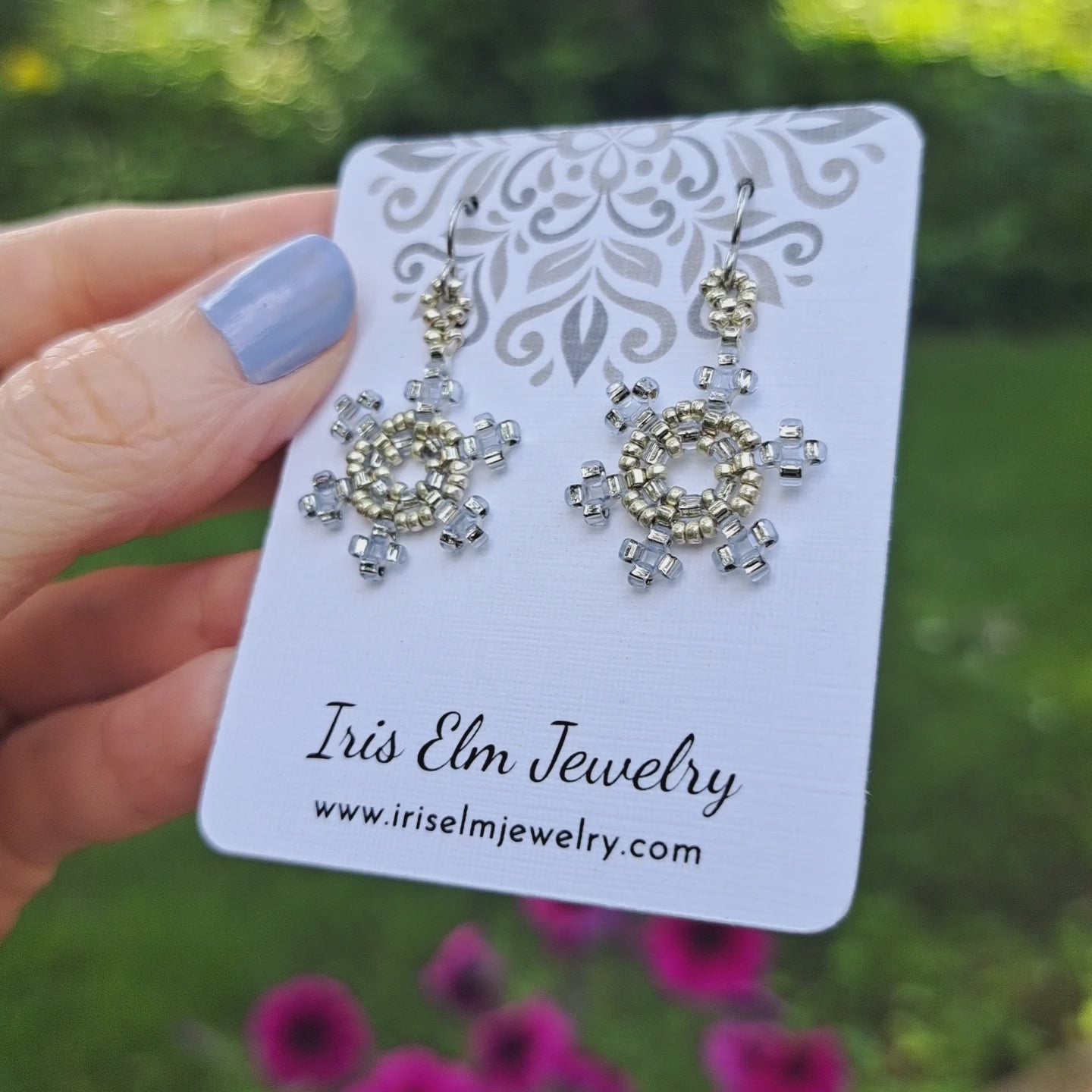pale blue and silver seed bead woven snowflake earrings on a branded Iris Elm Jewelry card held by hand