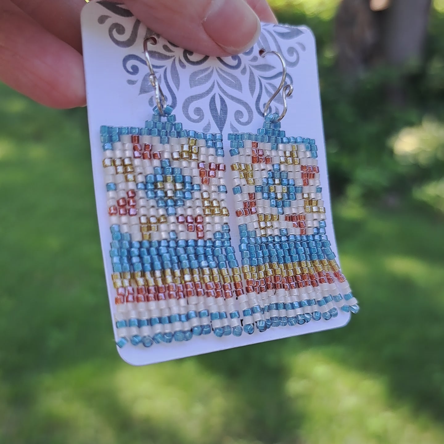 a pair of fringe quilt block earrings on card held by hand