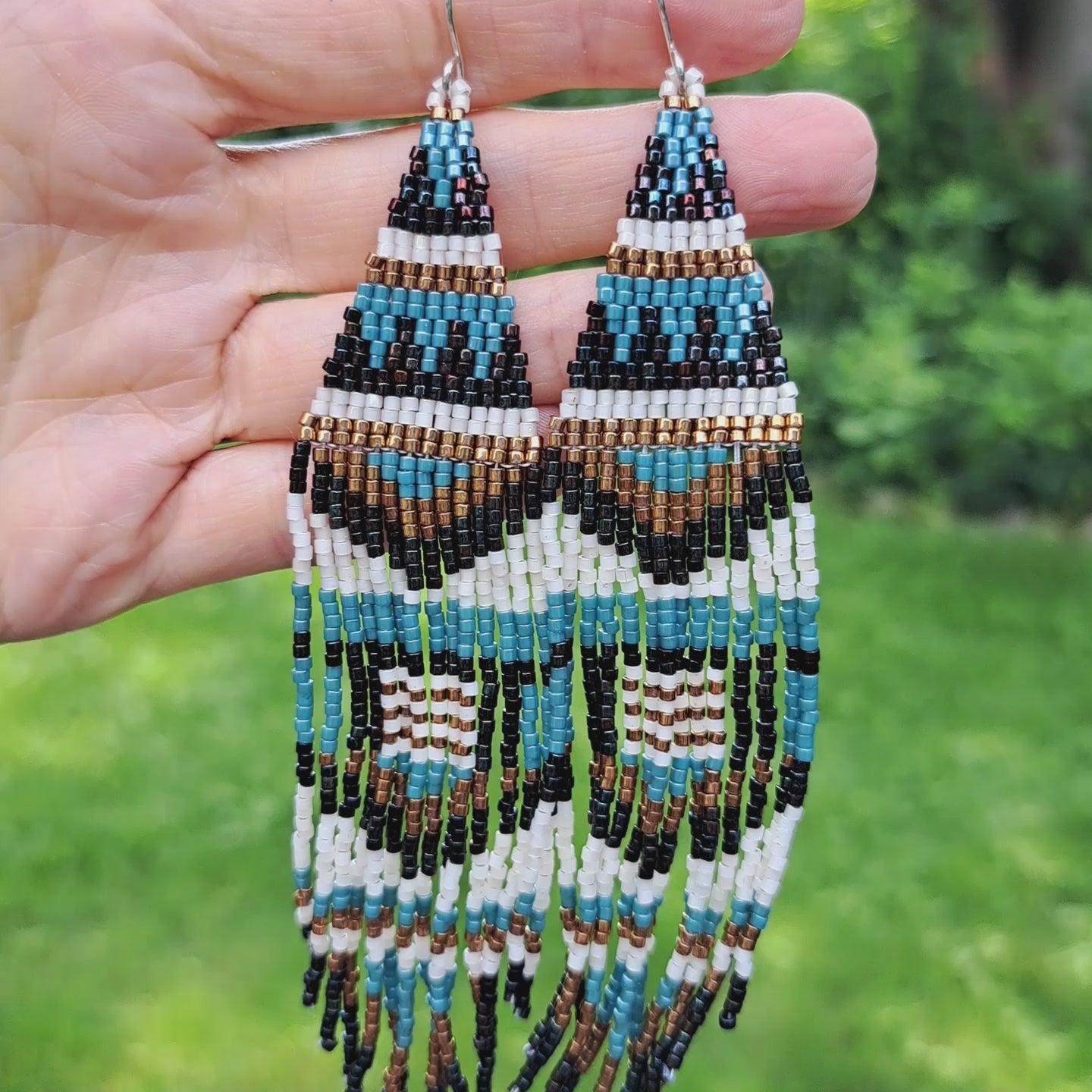 a pair of long seed bead fringe earrings with geometric pattern held in hand in outdoor setting