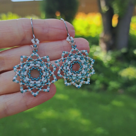 hand holding pair of mandala woven earrings with turquoise green, white and copper colored seed beads