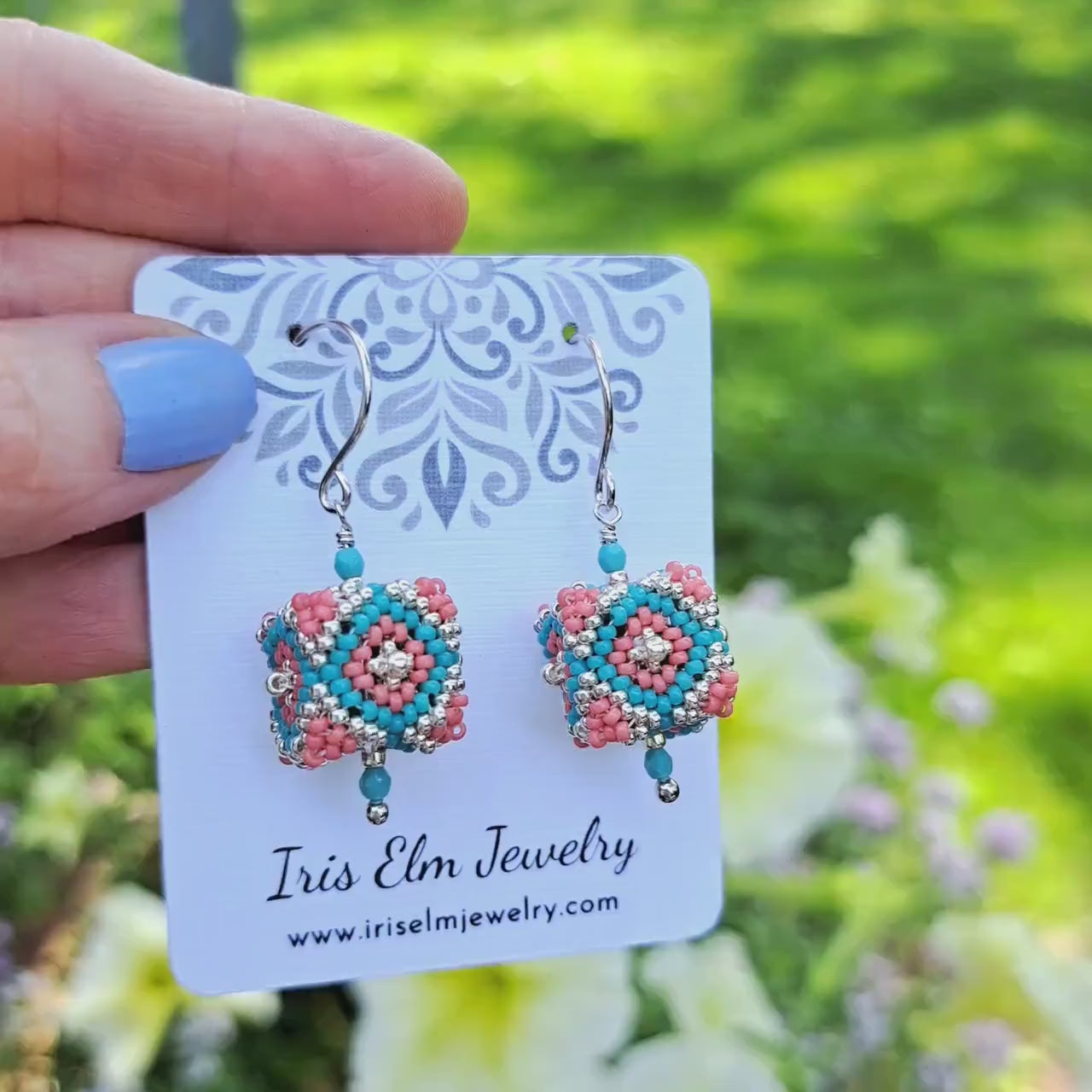 beadwork seed bead cube shaped earrings with silver, coral pink, and turquoise glass beads on 'Iris Elm Jewelry' card held by hand